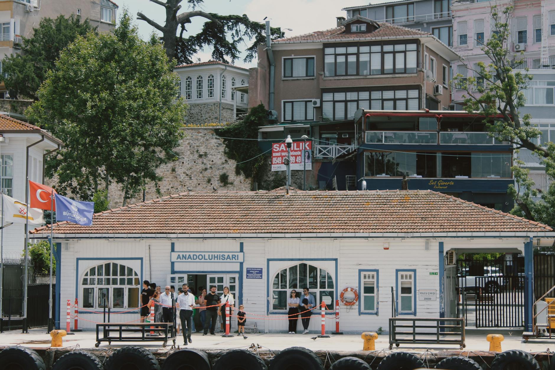 Passengers waiting outside the white wooden Anadoluhisarı ferry terminal building in Istanbul.