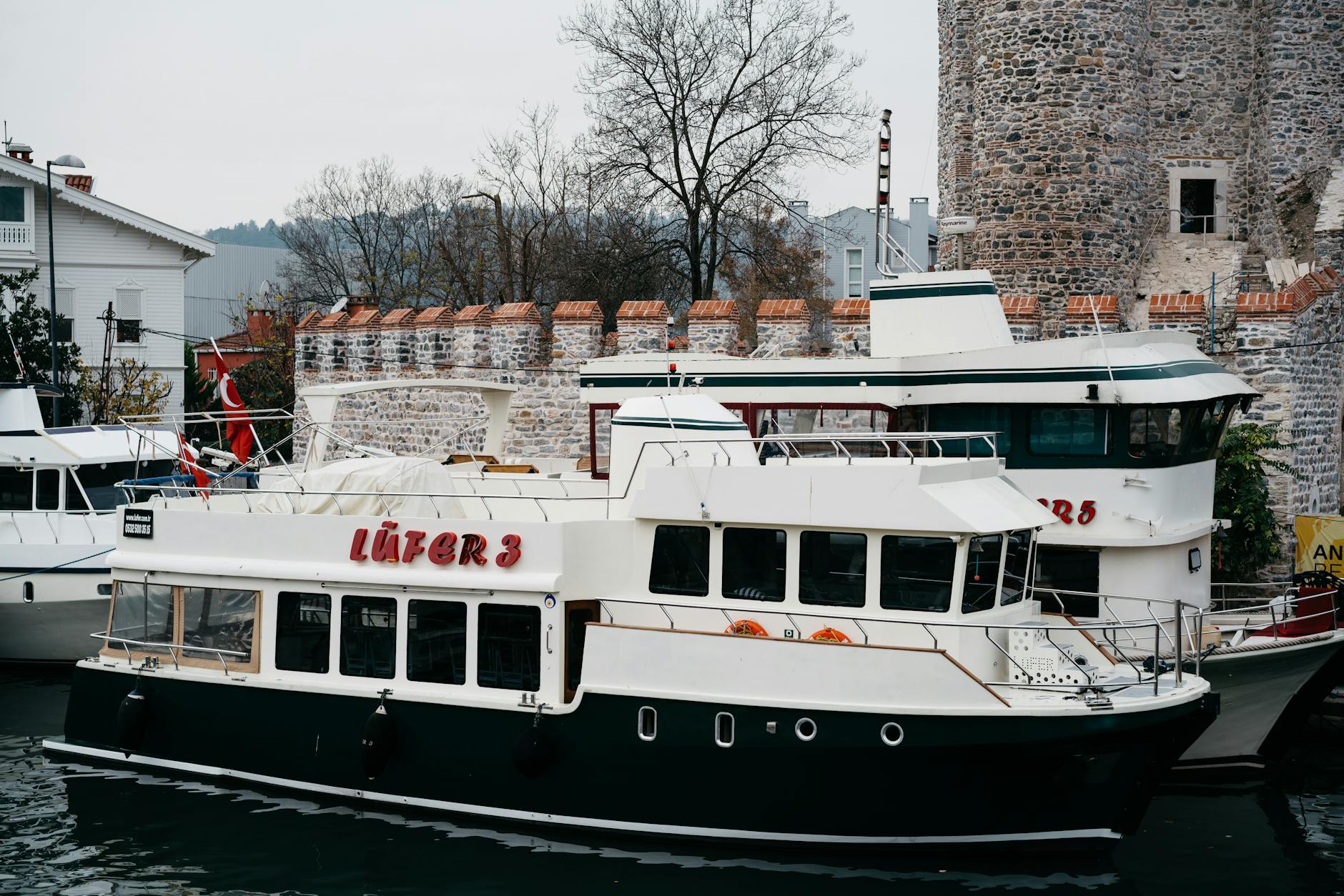 A white and blue boat docked near the historic stone walls of Anadoluhisarı.
