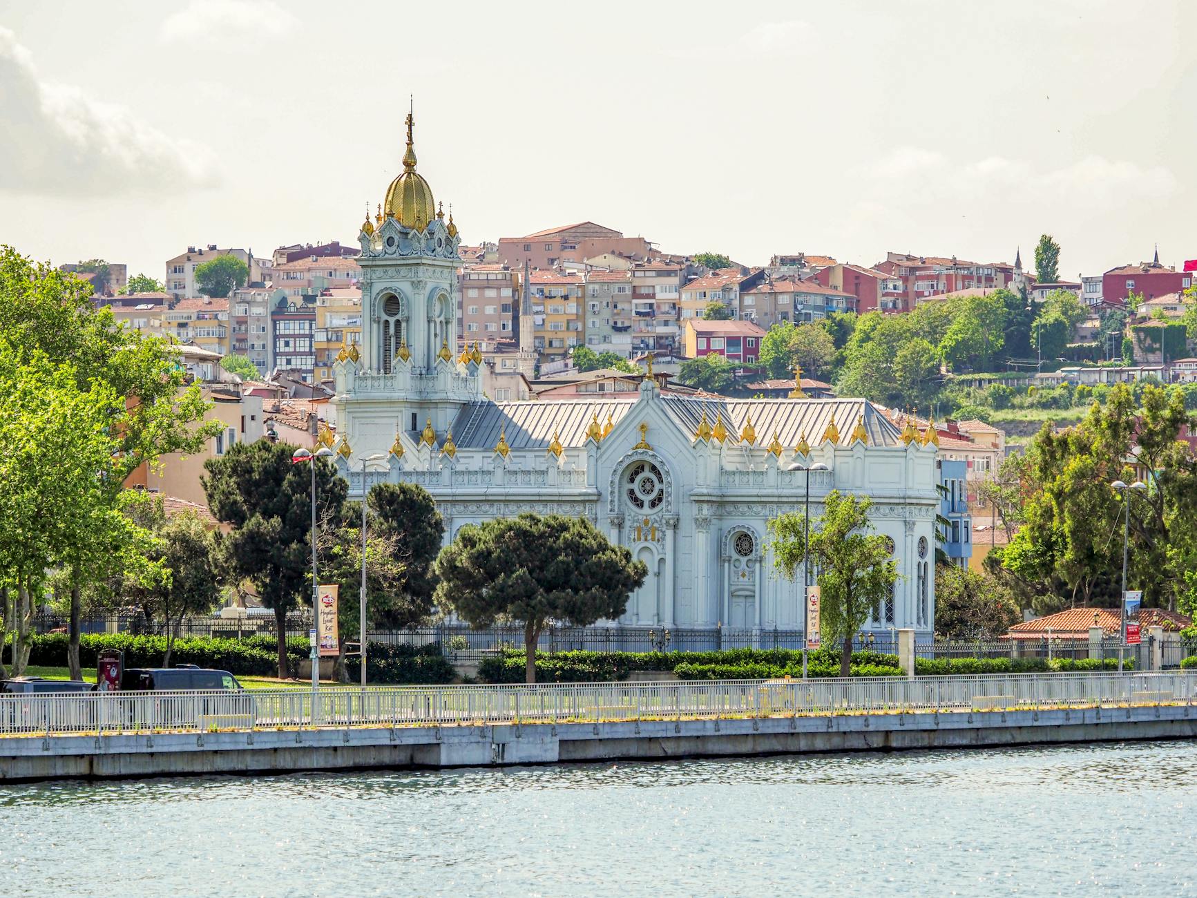 Exterior view of the Bulgarian St. Stephen Church (Iron Church) in Istanbul's Balat district, featuring its distinctive white facade and golden dome, seen across the water.