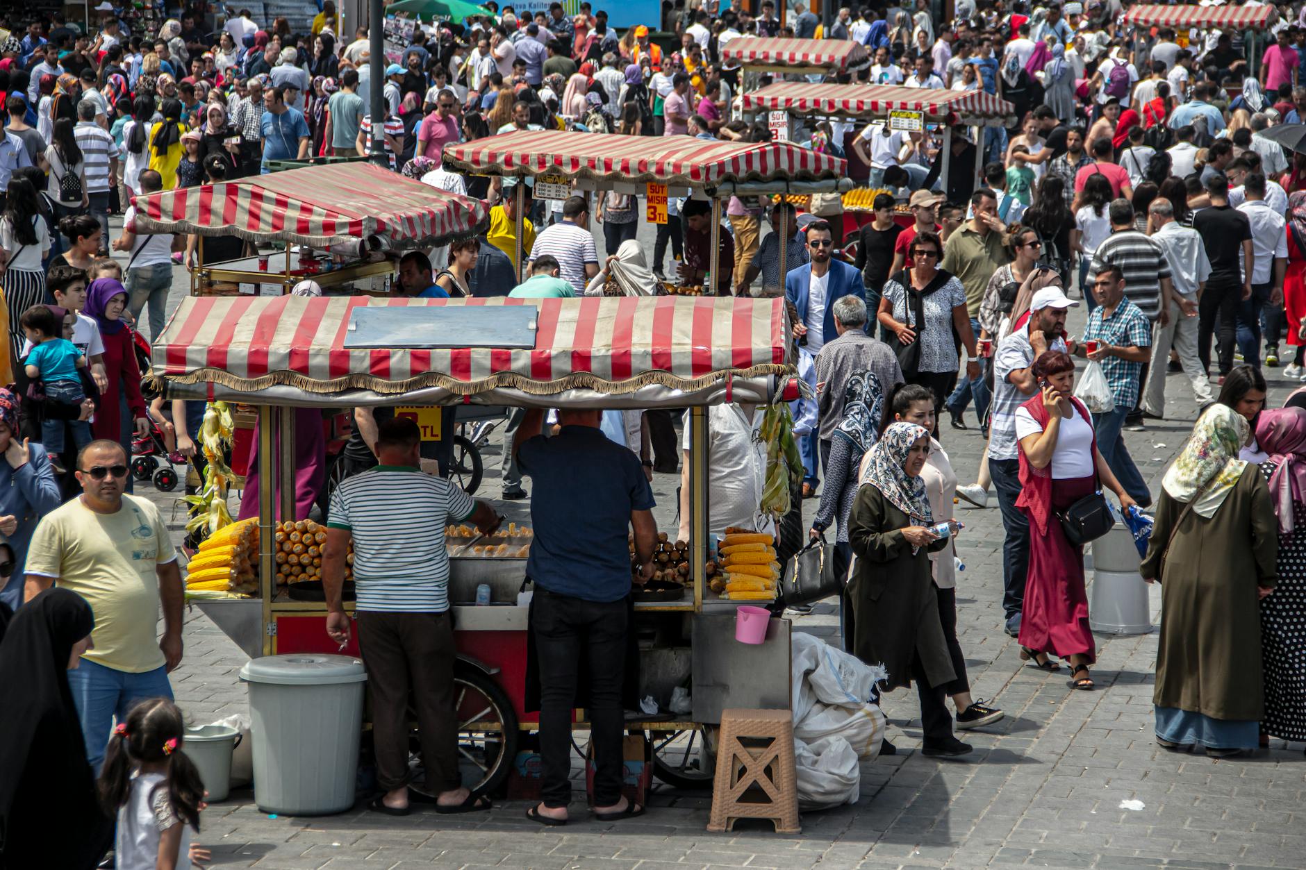 Many traditional red and white street food carts amidst a large crowd in Istanbul.