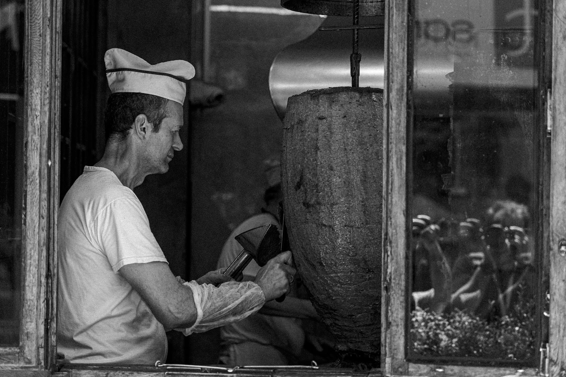 A professional chef carves thin slices of meat from a traditional vertical doner rotisserie.