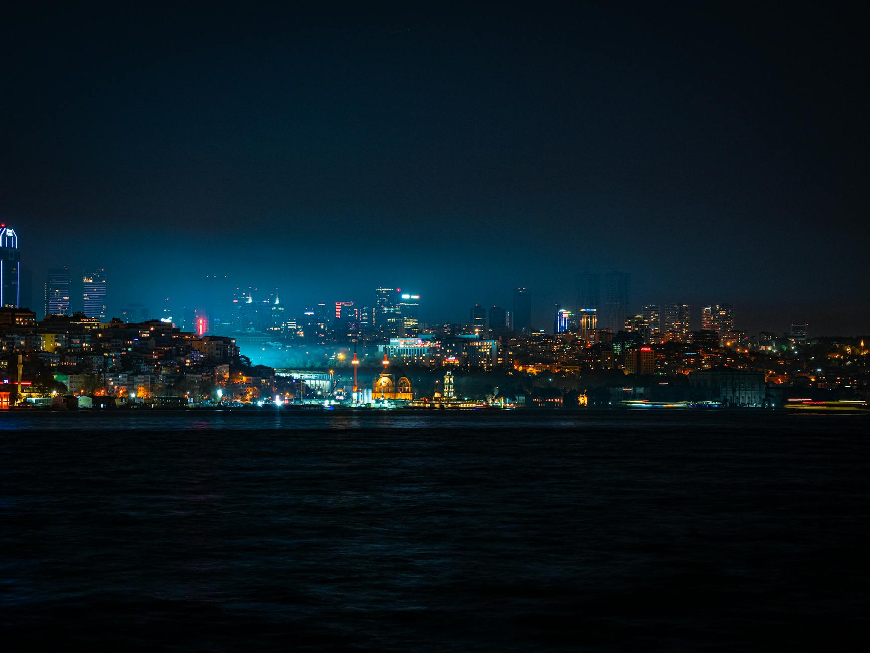 The city skyline glows across the dark waters of the Bosphorus at night.