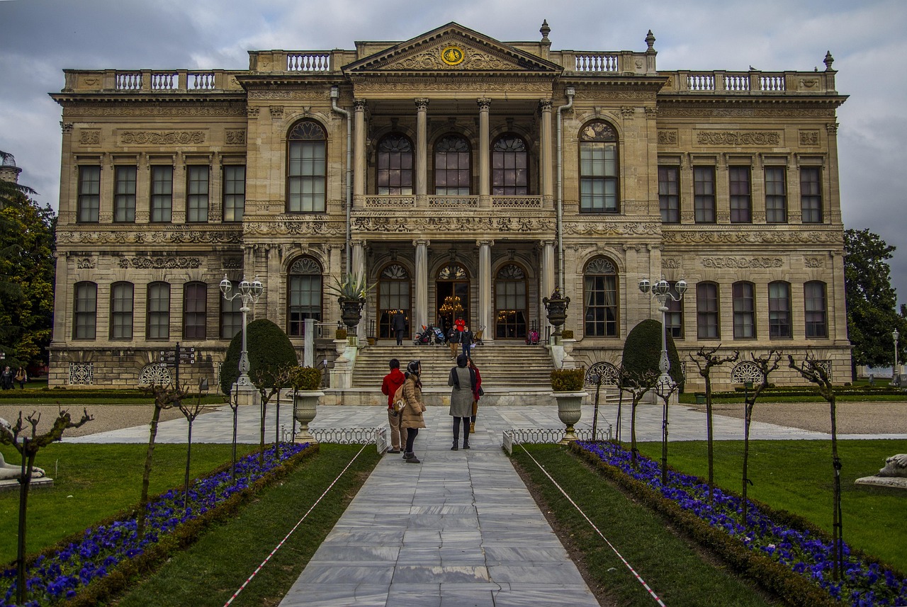 Tourists walking through the landscaped gardens toward the ornate entrance of Dolmabahçe Palace.