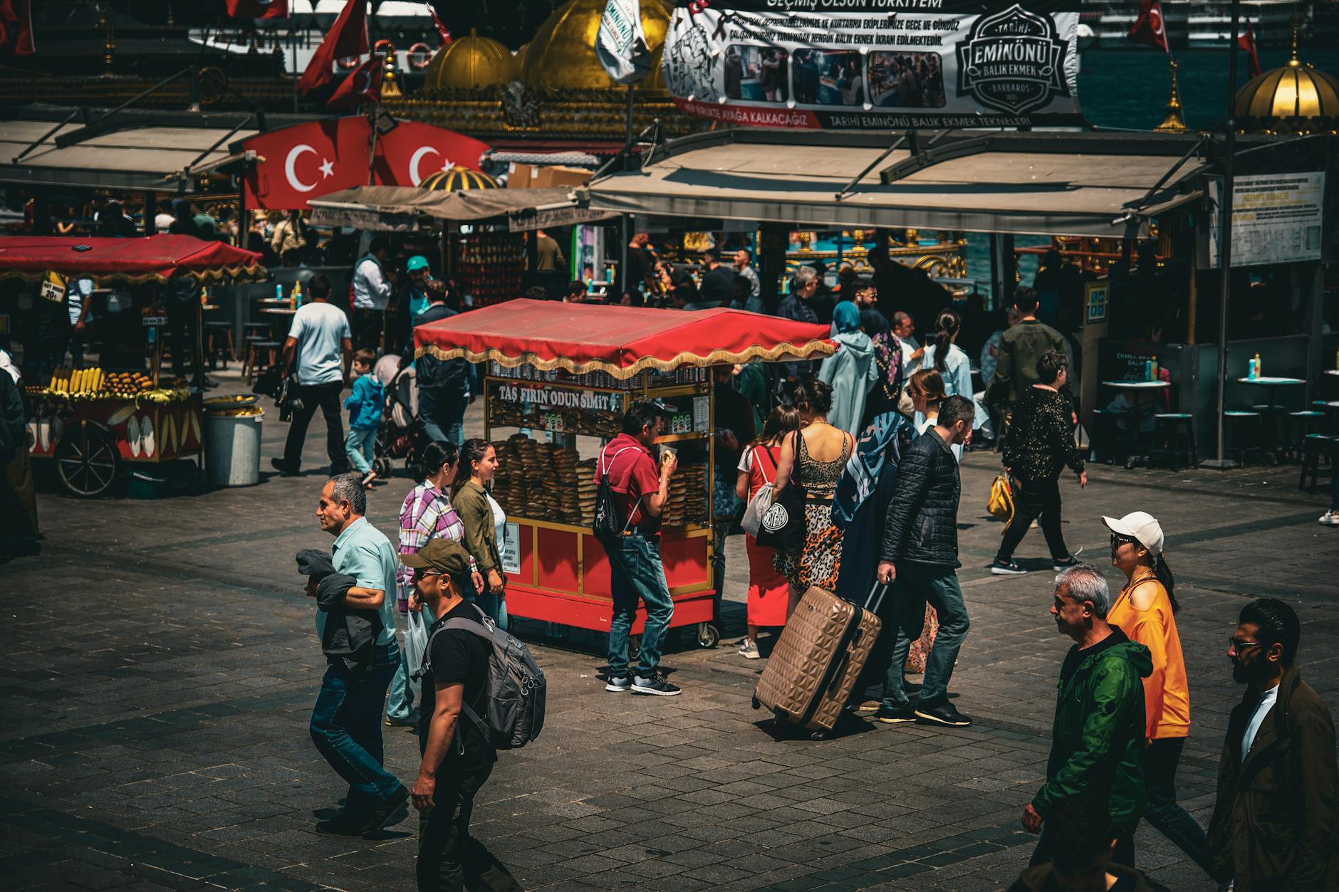 Crowded street market in Eminönü with traditional food stalls and Turkish flags.