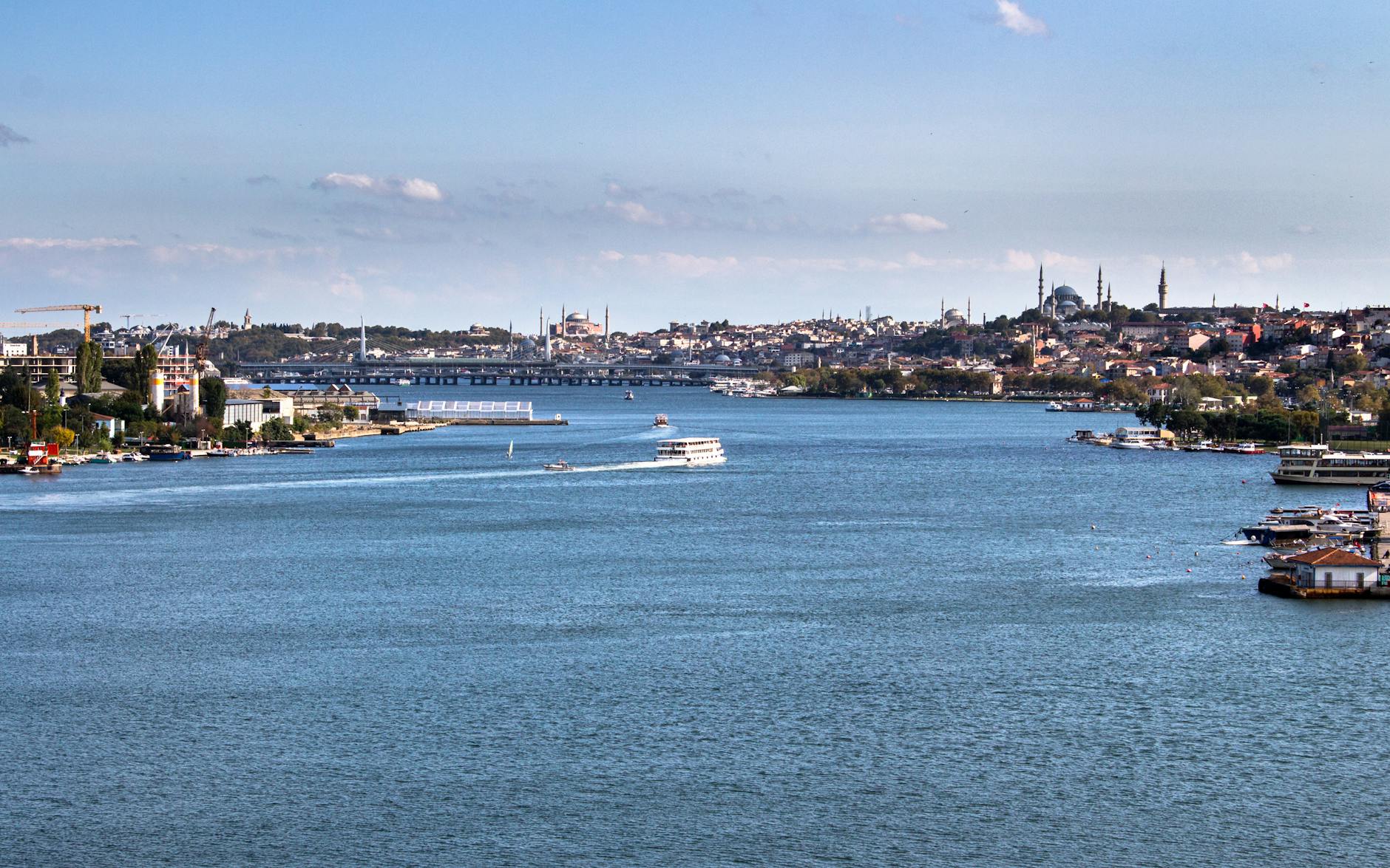 Panoramic view of the Golden Horn in Istanbul featuring ferries and historic mosque silhouettes.