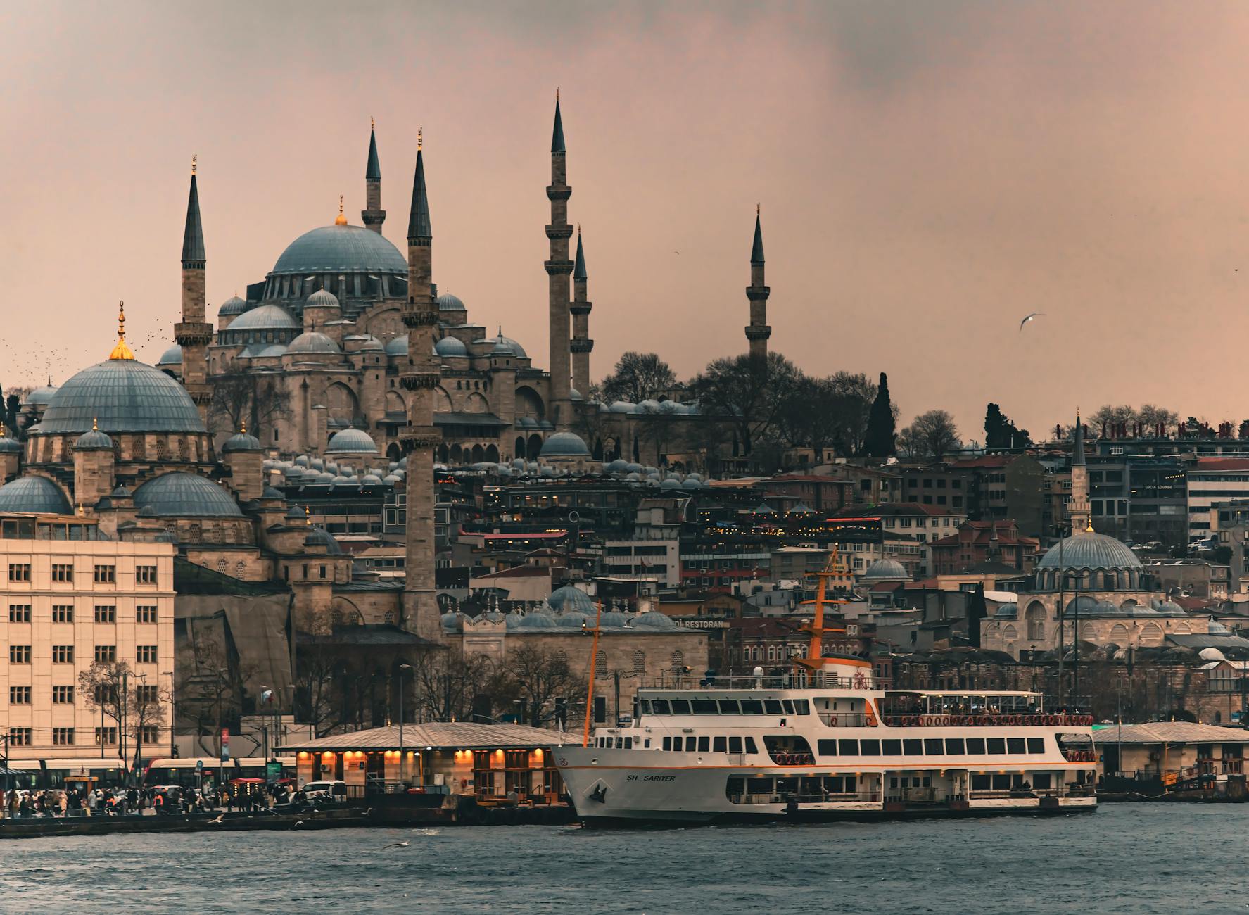 A white ferry cruises the Golden Horn with the iconic Süleymaniye Mosque in the background.
