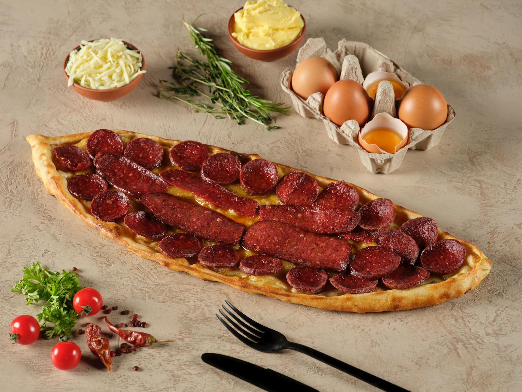 Professional shot of a boat-shaped pide loaded with sliced sucuk sausage.