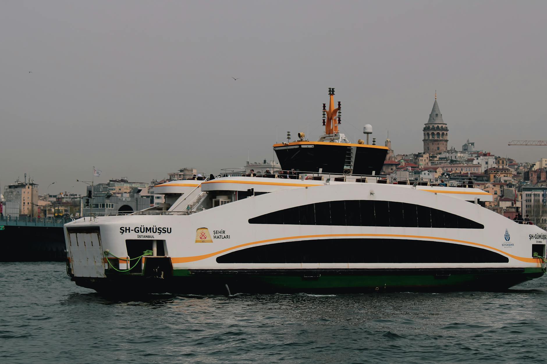 A white city ferry named Gumussu sails past the iconic Galata Tower in Istanbul.