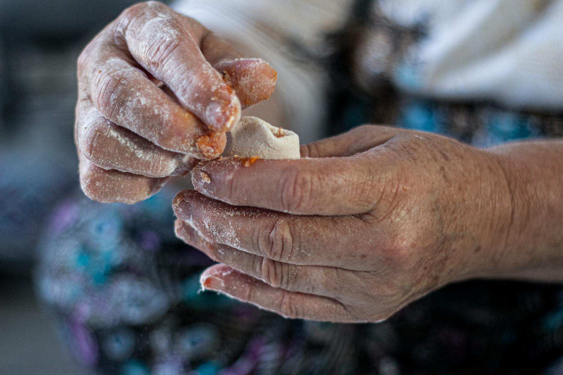 Aging hands covered in flour carefully folding a small piece of dough for a dumpling.