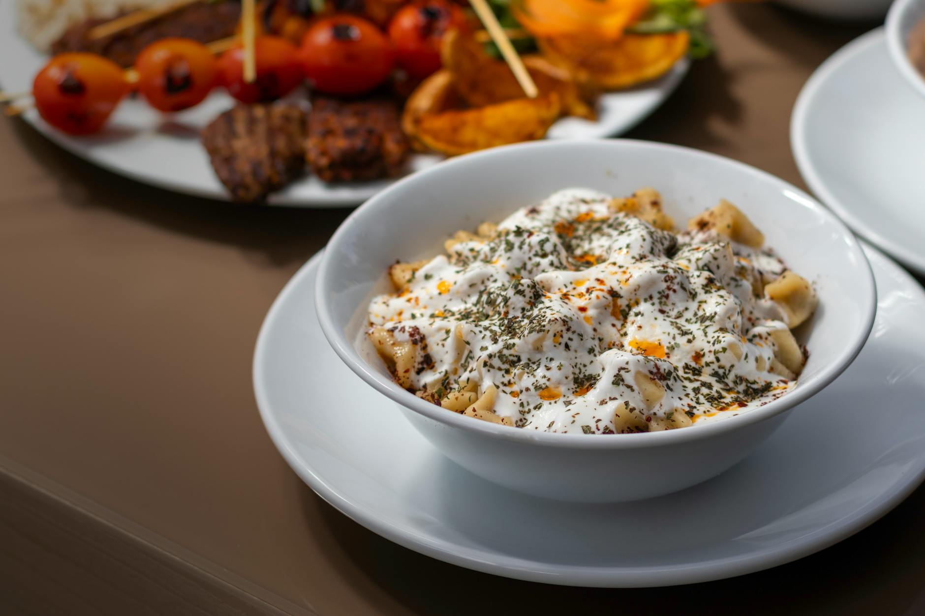 A bowl of traditional Turkish manti topped with creamy garlic yogurt and red spices.