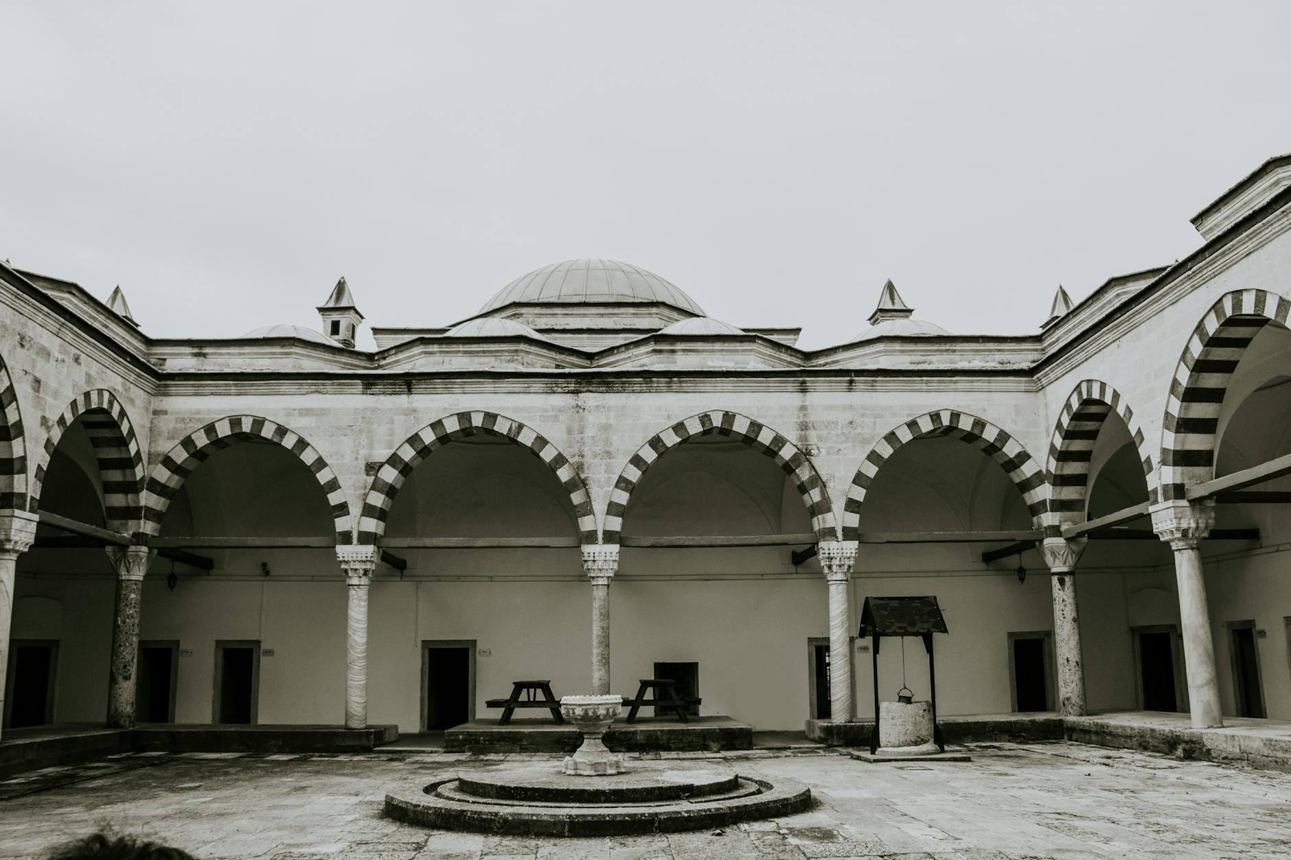 The stone courtyard of a historic medrese building with arched walkways and benches.