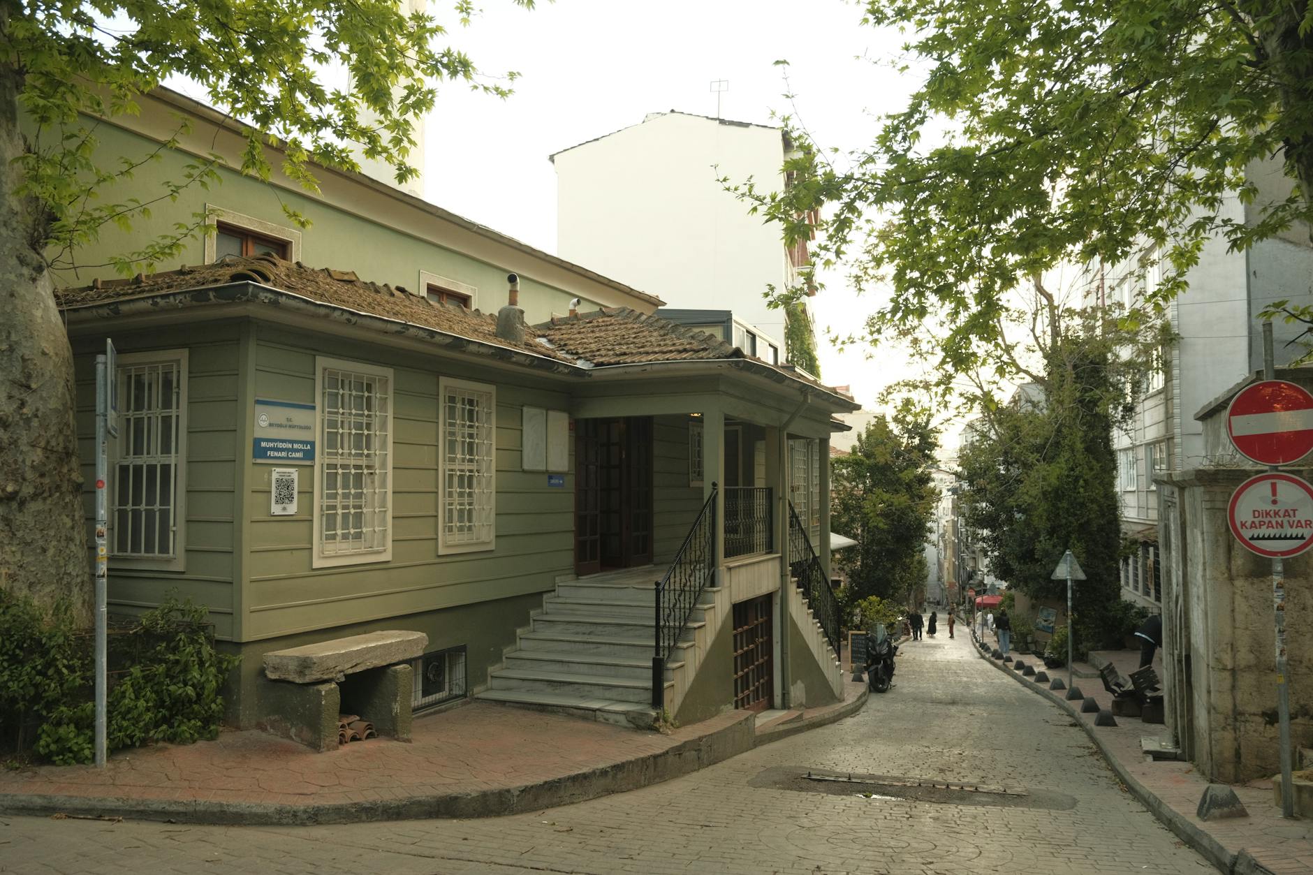 A historic green wooden mosque sits on a quiet, sloping cobblestone street in Çukurcuma.