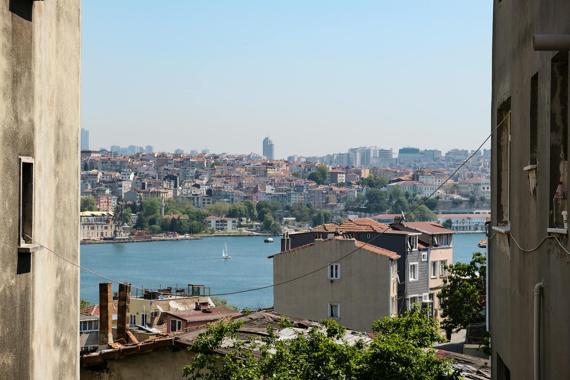 View of the bustling Istanbul cityscape across the blue water, framed by adjacent buildings, highlighting the dense urban landscape of the city.