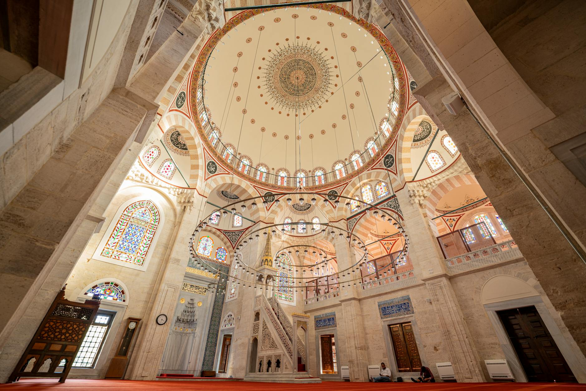 Spacious interior of Kilic Ali Pasha Mosque featuring grand chandeliers and colorful stained glass windows.