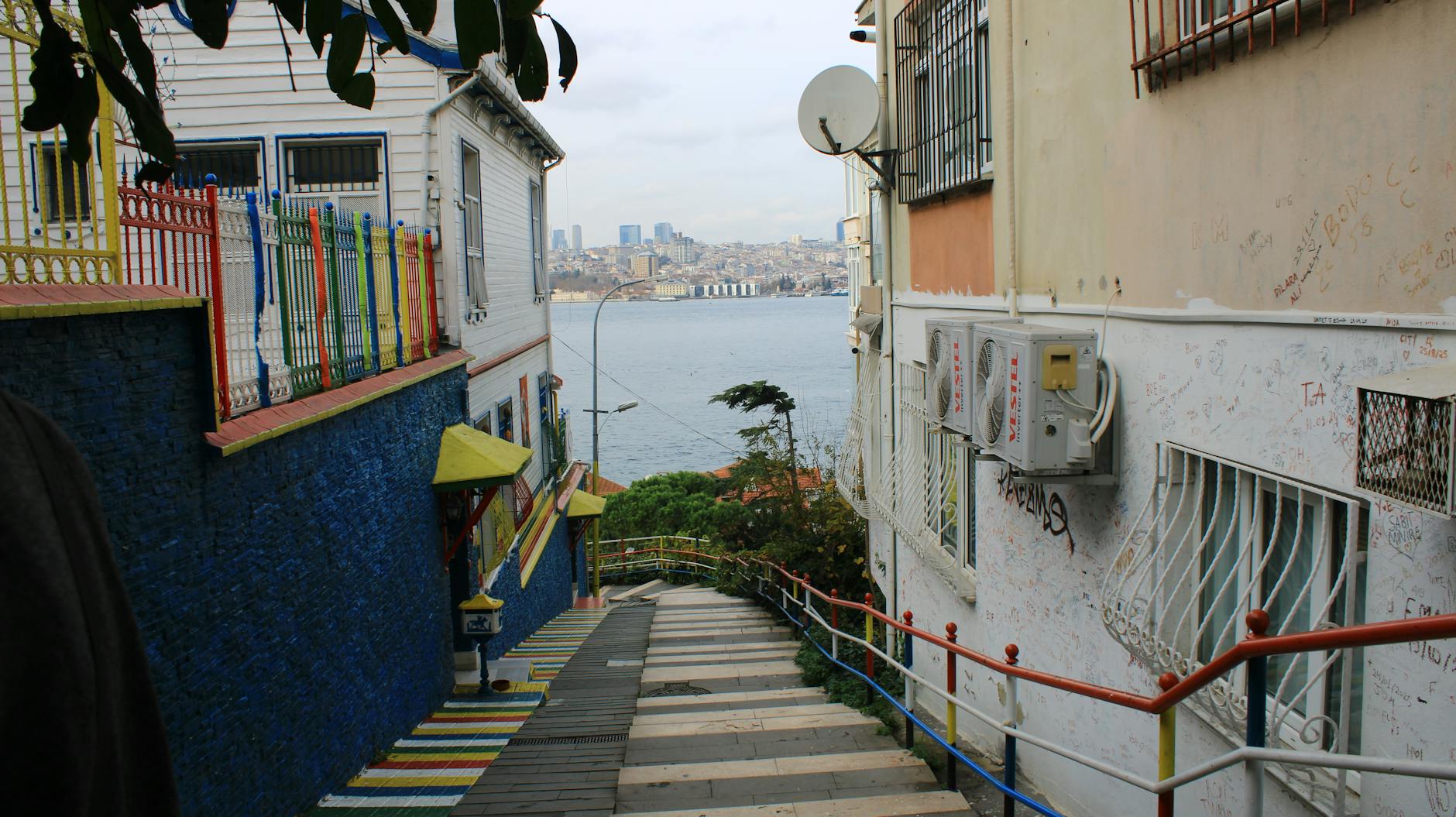 Colorful staircase street in Kuzguncuk descending towards the Bosphorus strait with the Istanbul skyline in the distance, reflecting Istanbul culture.