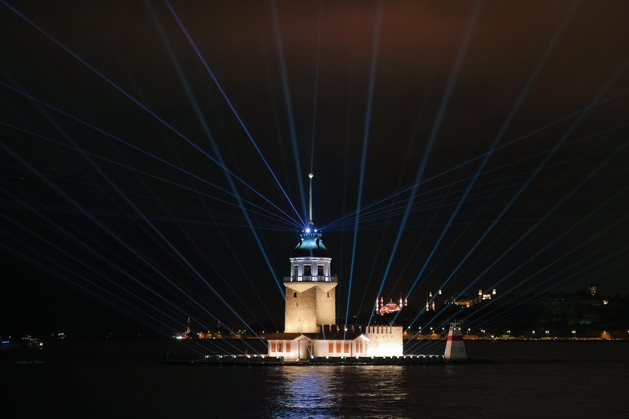 The illuminated Maiden's Tower stands in the Bosphorus with blue laser beams at night.