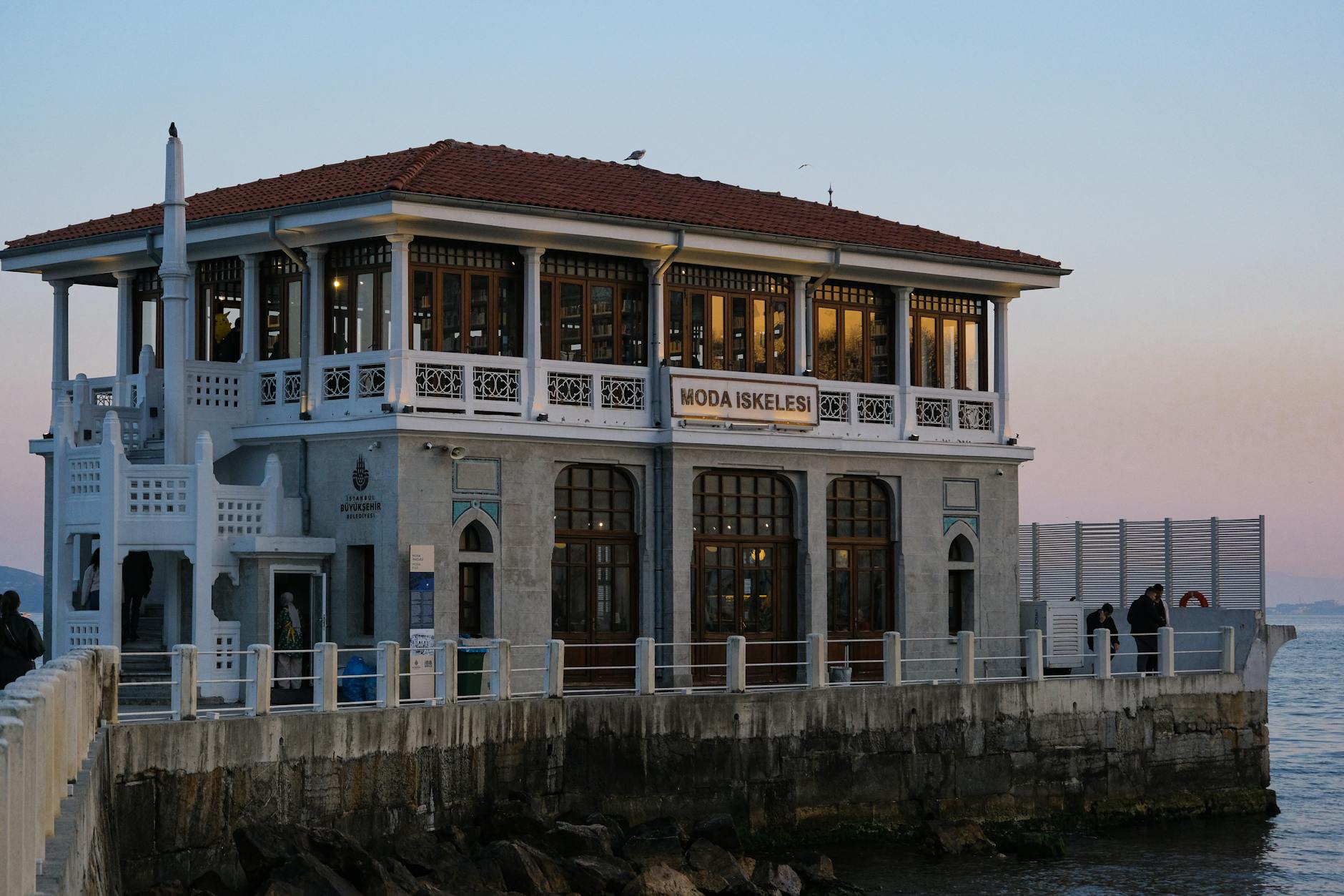 The historic Moda İskelesi (Moda Pier) building in Kadıköy, Istanbul, featuring white balconies and a red tile roof at dusk, a key spot on the Asian side of Istanbul tourism.