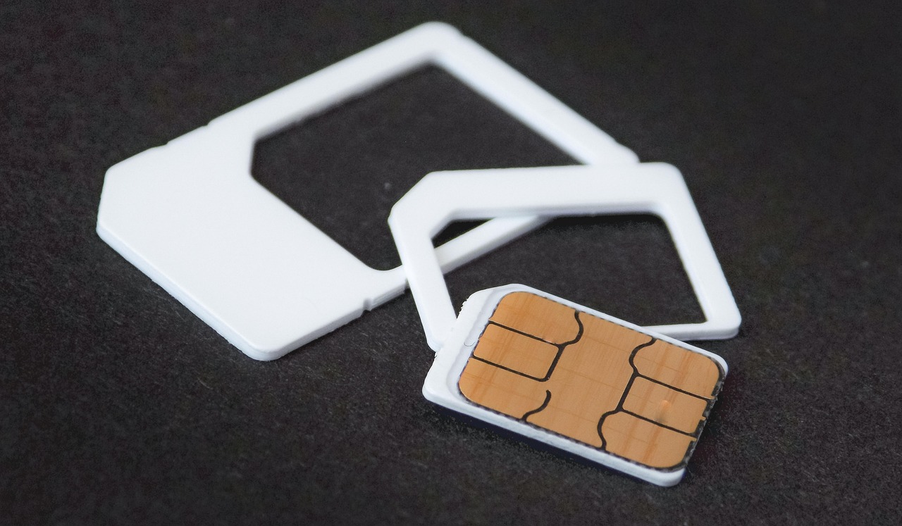 A nano SIM card rests beside white plastic adapters on a dark surface.