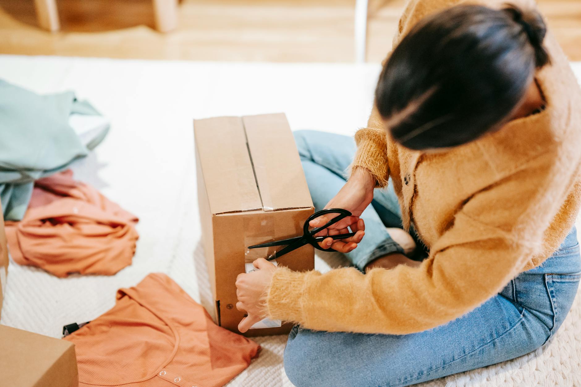 A person carefully prepares a box for shipment using tape and scissors.