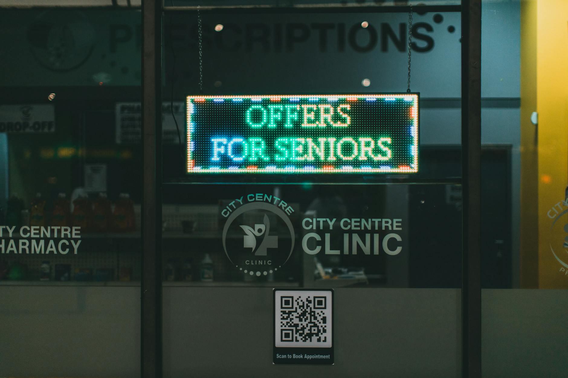 An illuminated pharmacy sign at night displaying offers for seniors.