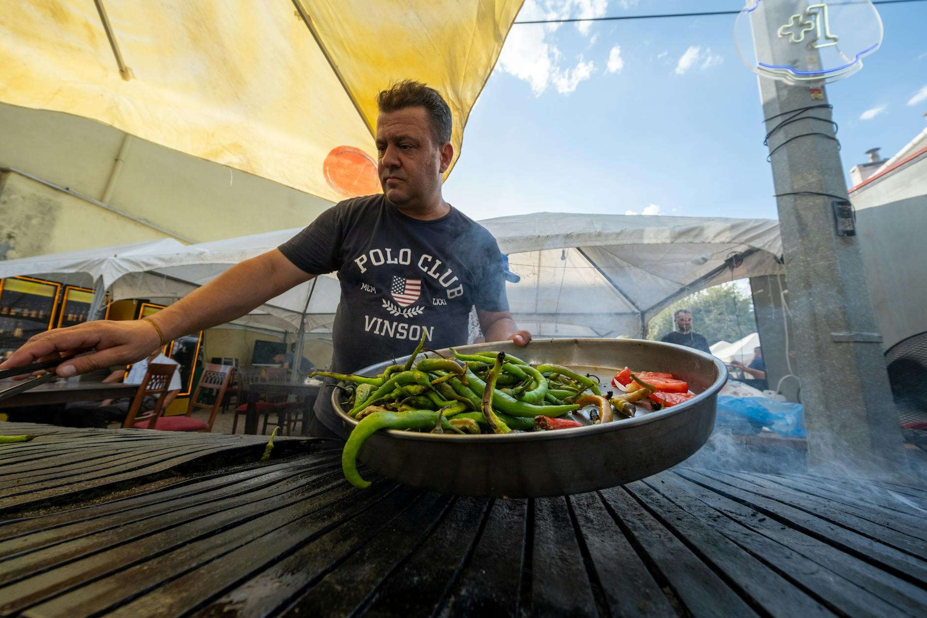 A cook prepares a large tray of roasted green peppers to accompany spicy meat wraps.