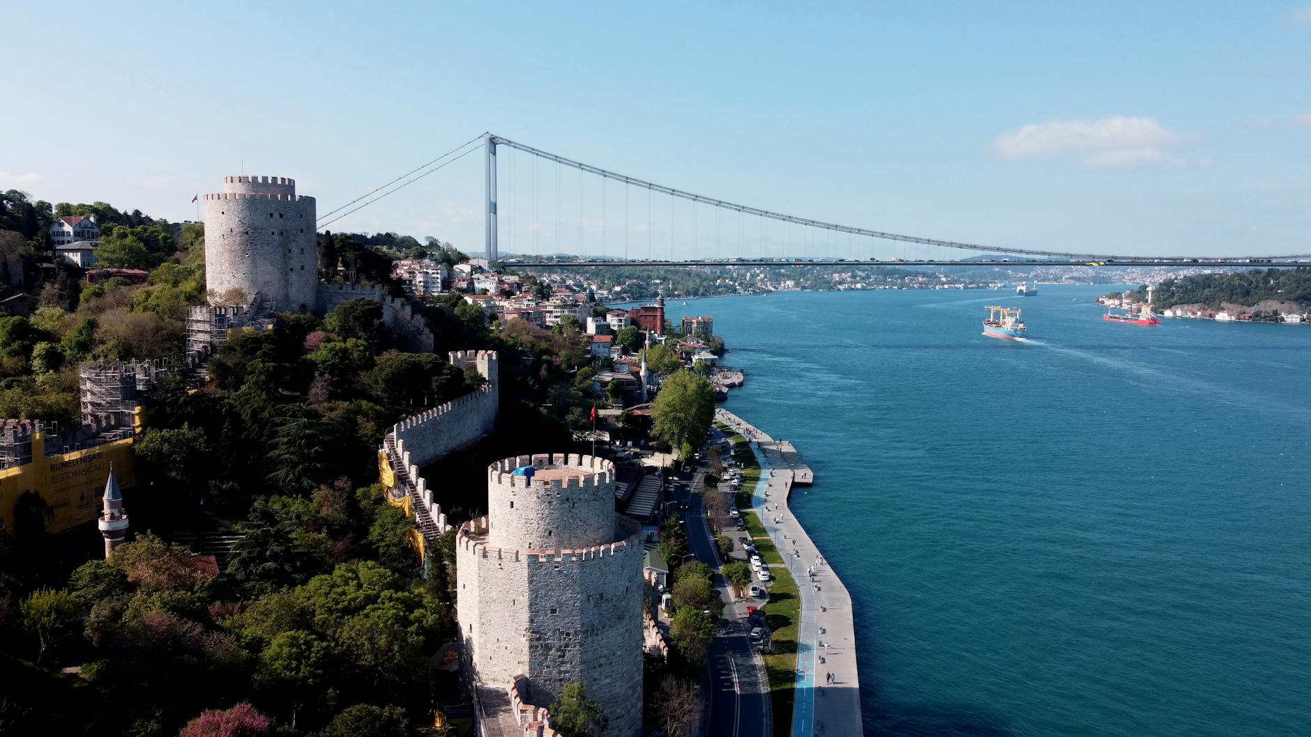 Aerial view of Rumeli Hisarı fortress towers next to the Bosphorus strait with ship traffic and the Fatih Sultan Berk Bridge in Istanbul.