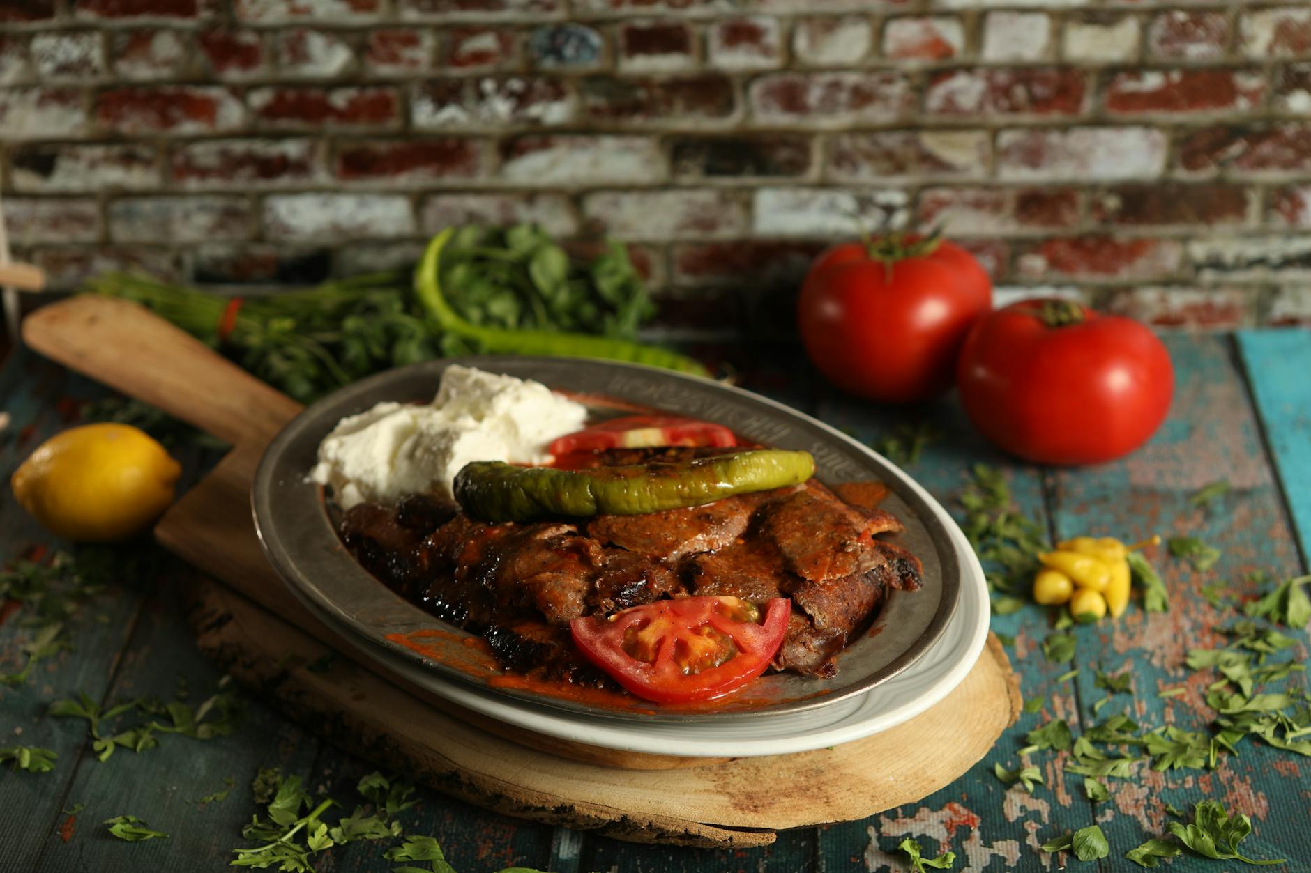 A plate of sizzling Iskender kebab with yogurt, tomato sauce, and grilled pepper.
