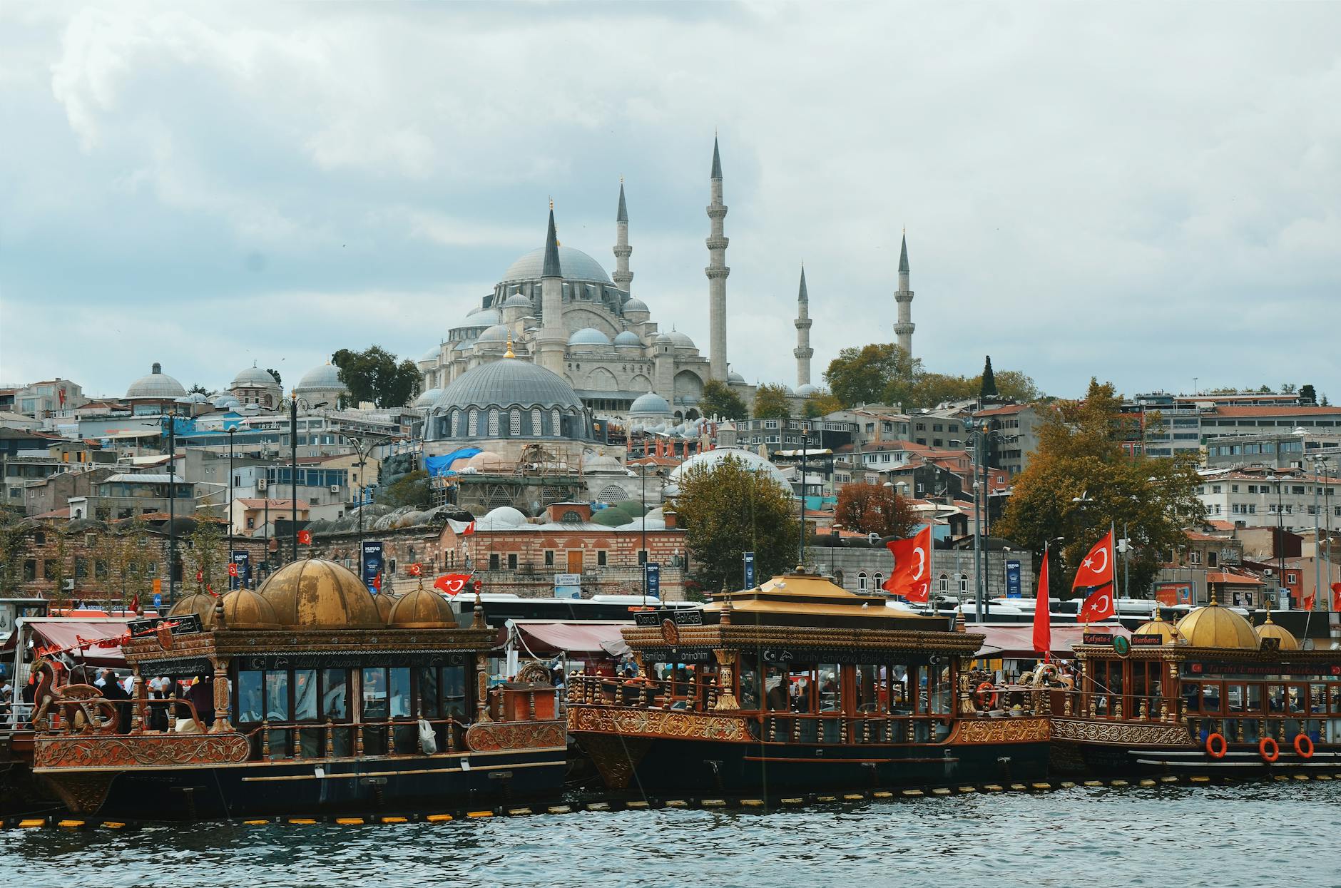 View of the historic Suleymaniye Mosque towering over the Golden Horn with ornate tour boats docked below, a popular Istanbul tourism sight.