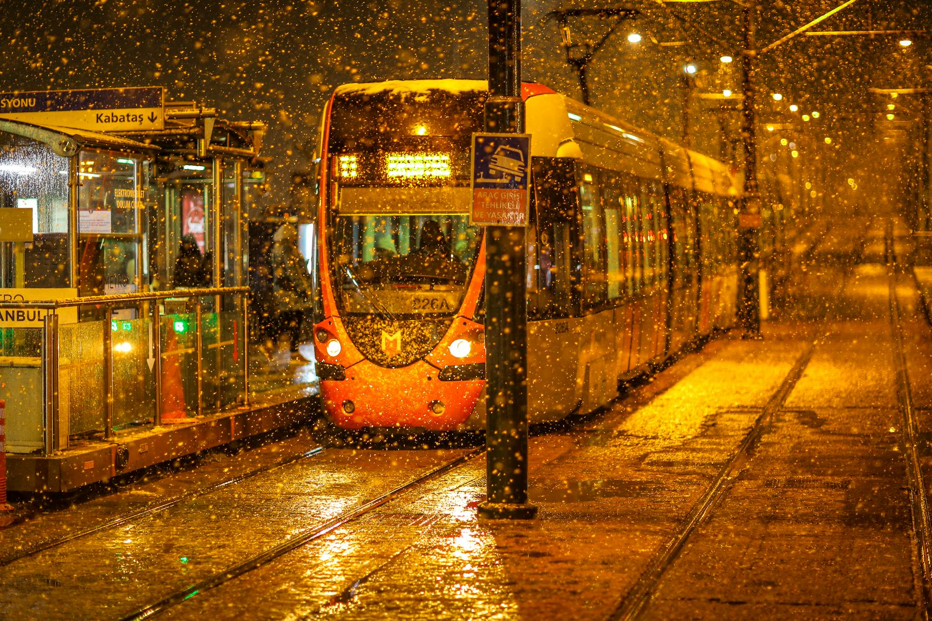 A modern T1 tram arrives at the Kabataş station during a heavy snowstorm at night.