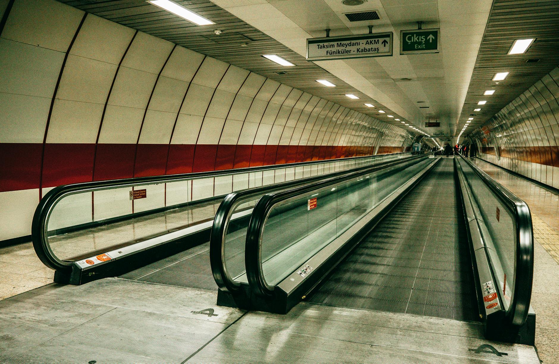 A long moving walkway leads toward the Taksim Square exit inside an Istanbul metro station.
