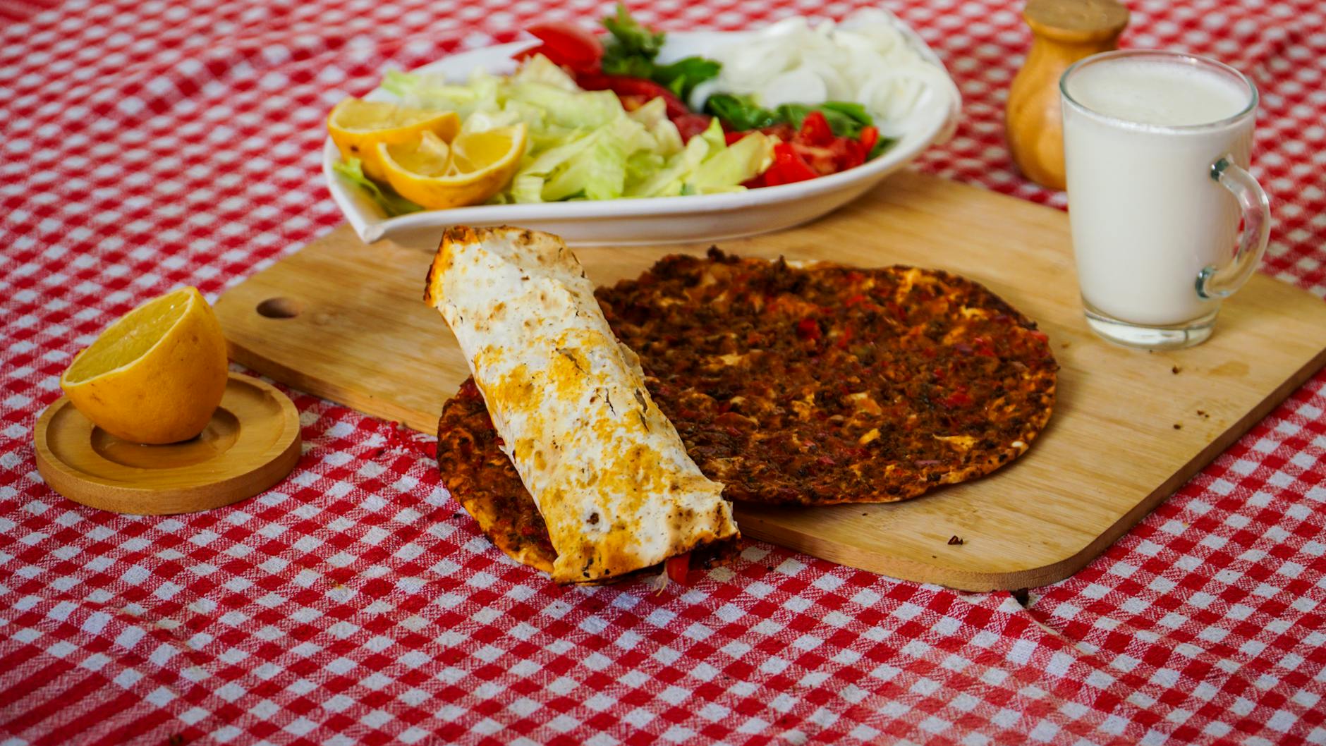 Two thin crust lahmacuns served with fresh salad and a glass of cold ayran.