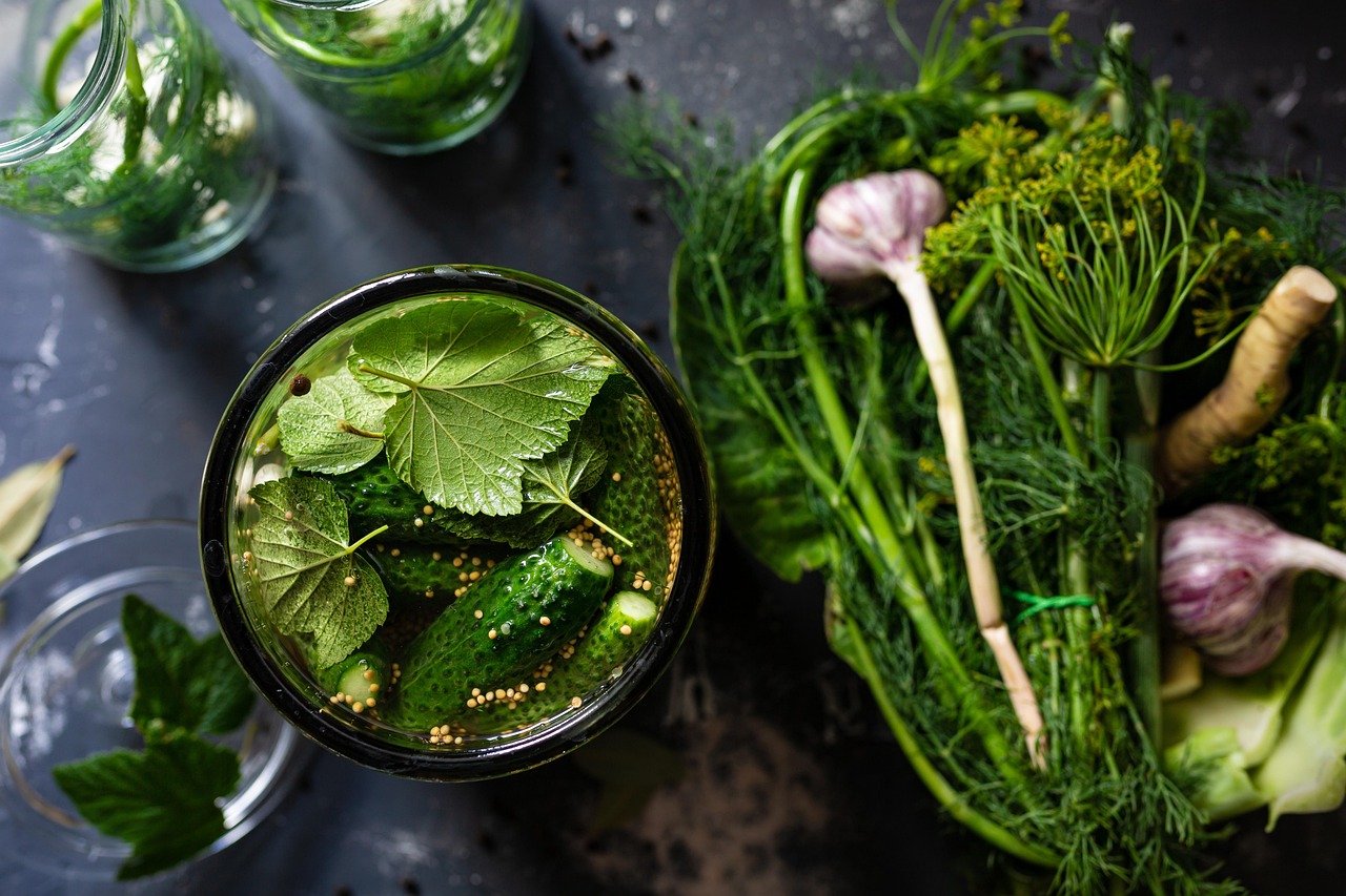 A glass jar filled with fresh cucumbers, grape leaves, and garlic for traditional pickling.