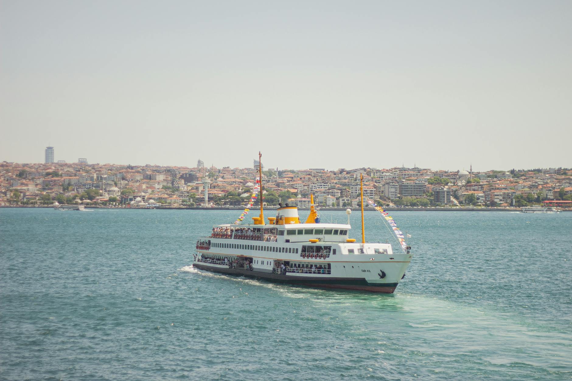 A traditional white and yellow passenger ferry sailing across the blue Bosphorus waters.