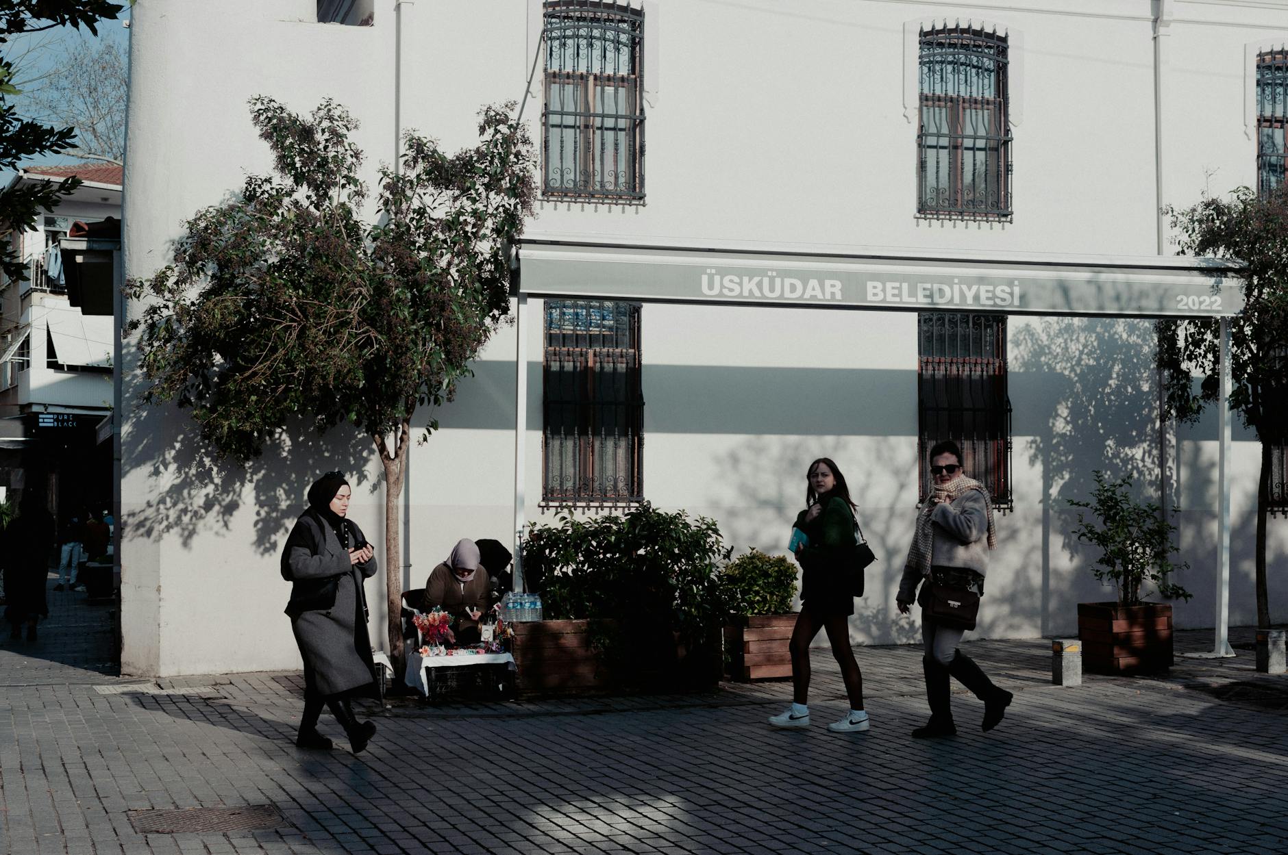 Pedestrians walk past the Üsküdar Municipality building on a bright sunny day.