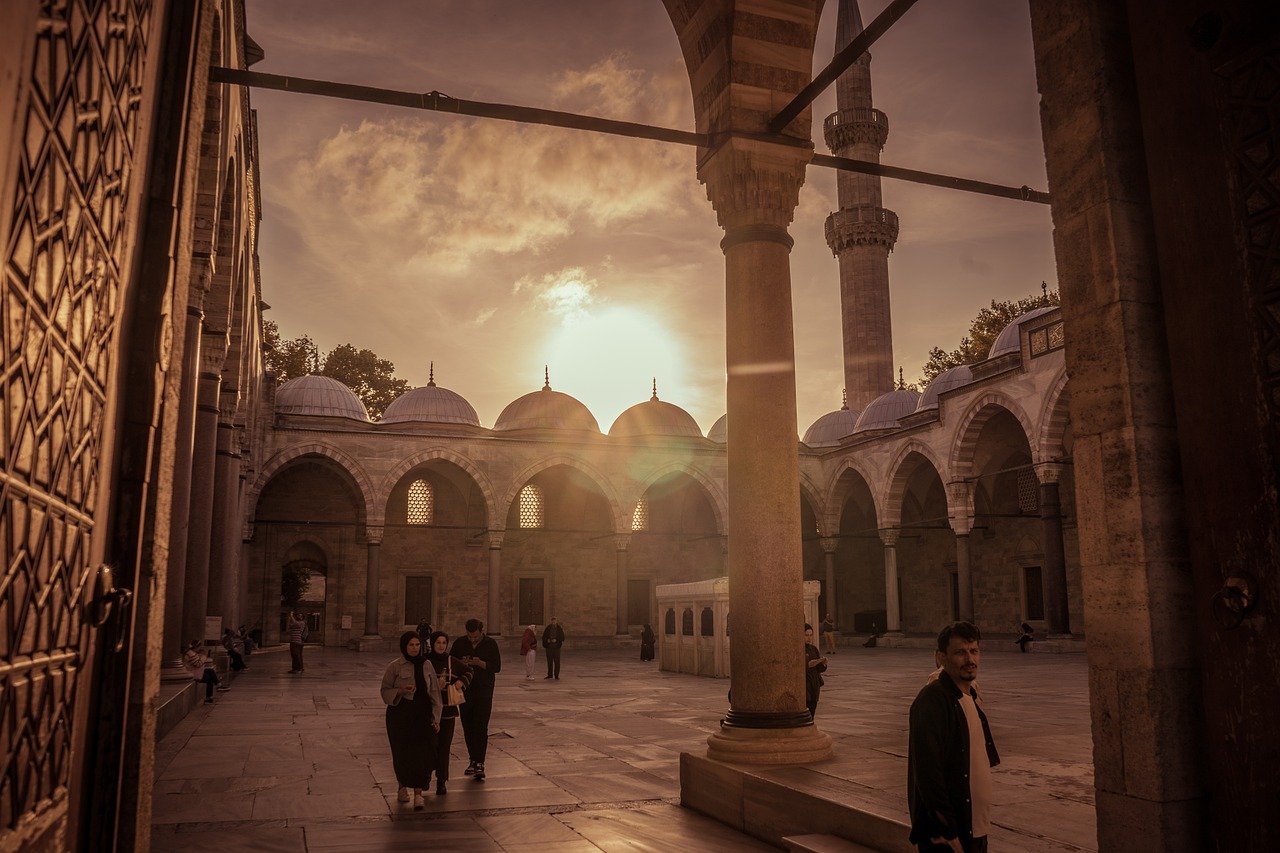 People walking through the sunlit courtyard of Yavuz Selim Mosque at dusk.